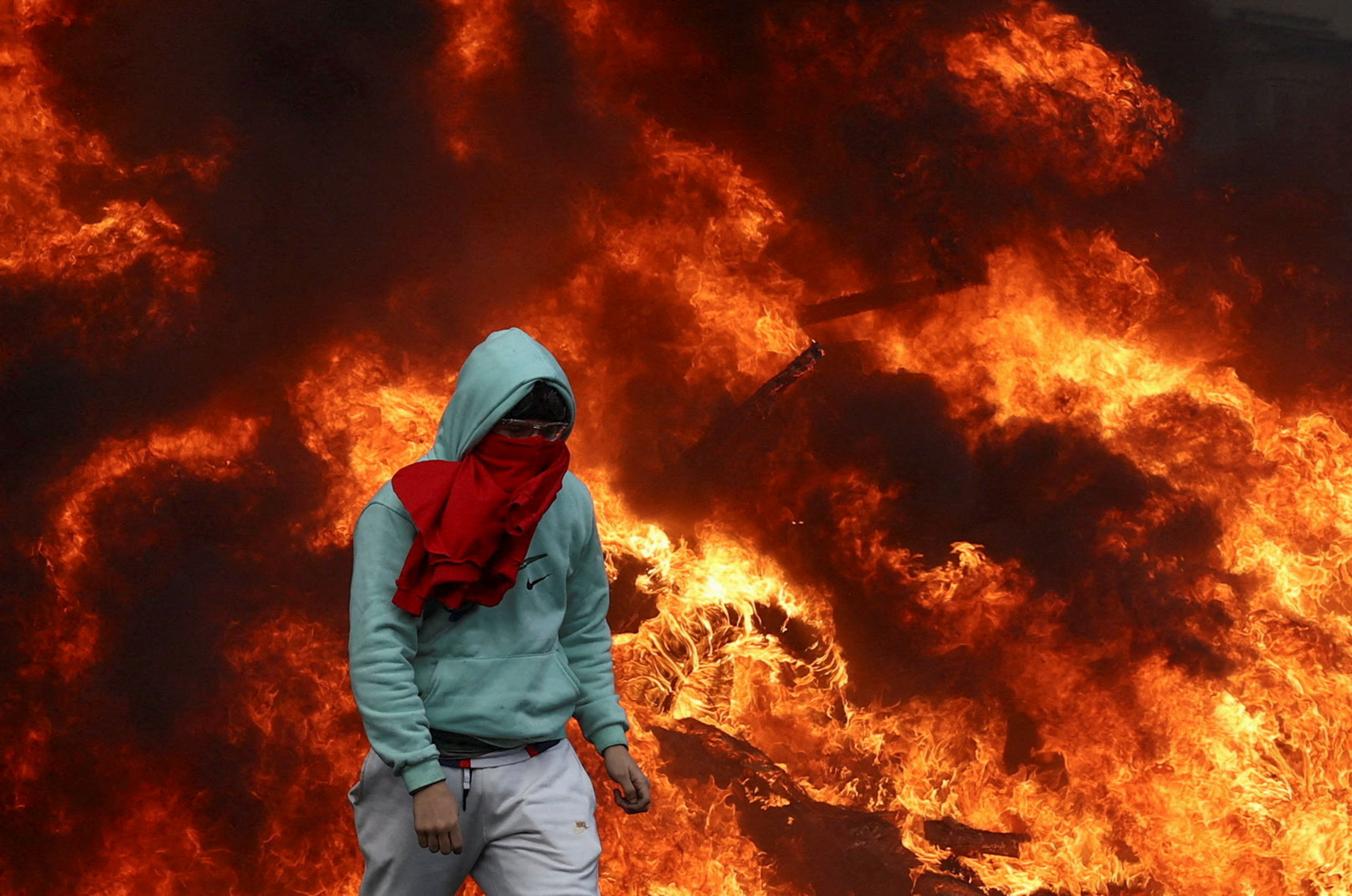 A protester walks next to burning tires that send up a wall of flames.