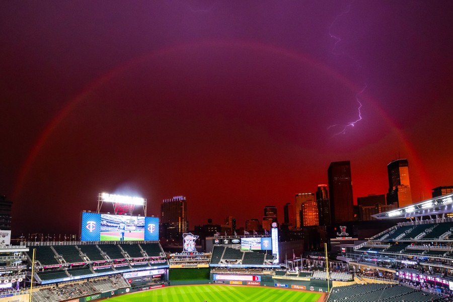 Lightning strikes and a rainbow appear in a dark sky above a baseball stadium.