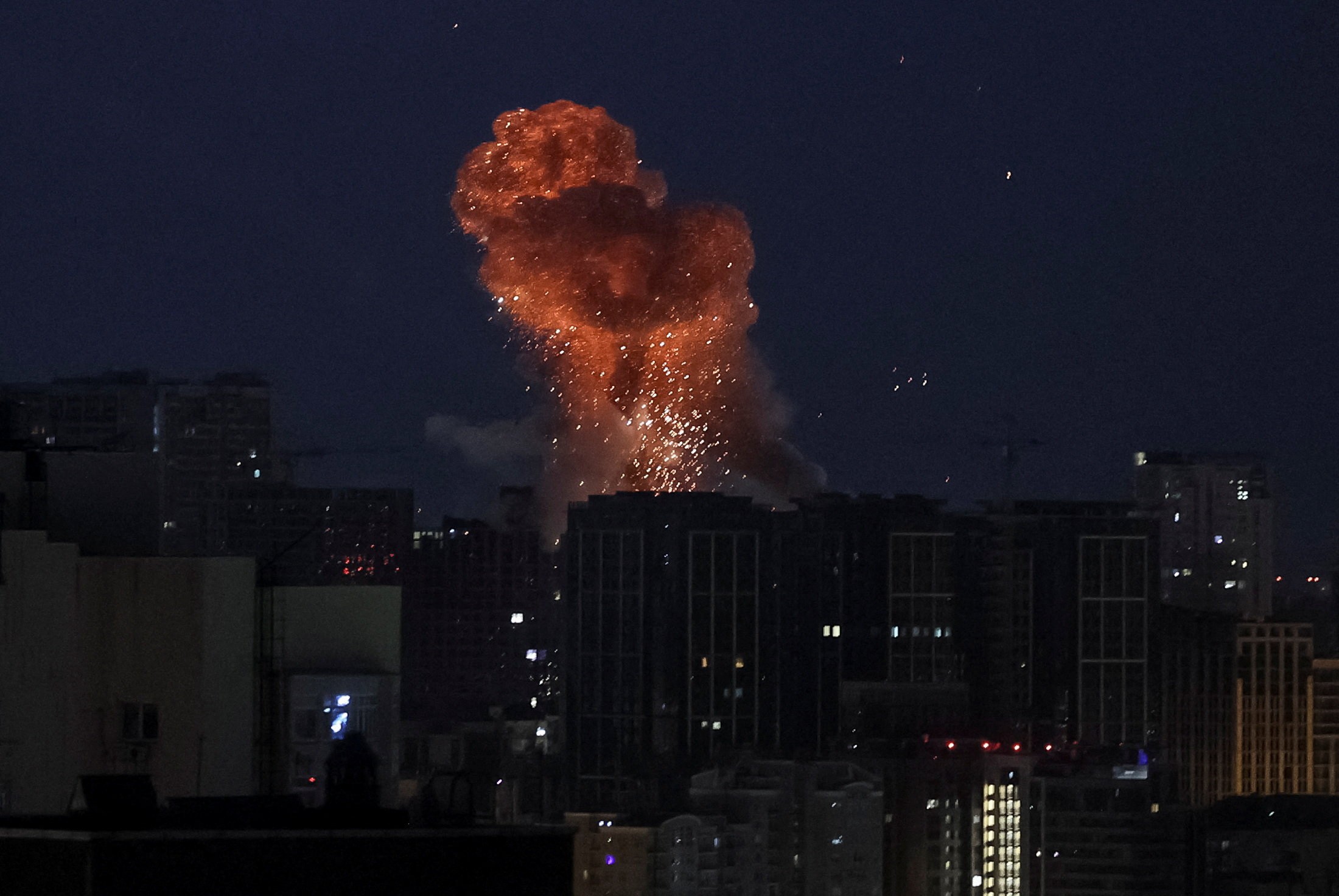 Smoke and sparks rise above a missile strike in a city, seen at night.