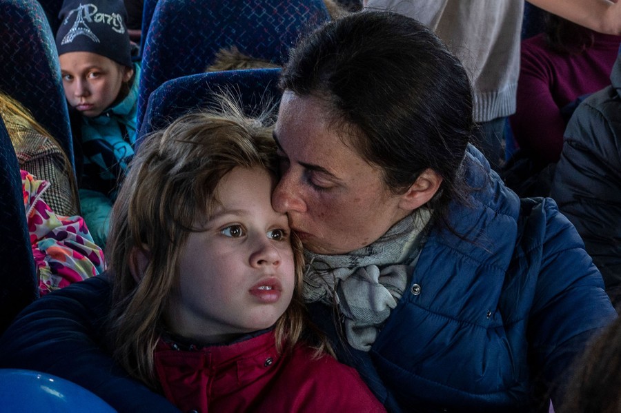A person kisses the forehead of a child aboard a crowded bus.