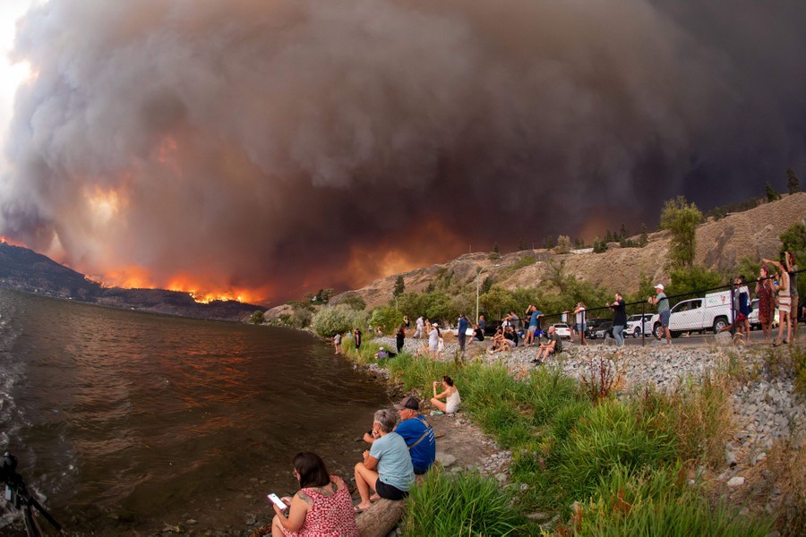 People gather along a waterfront to watch wildfires on a nearby ridge.