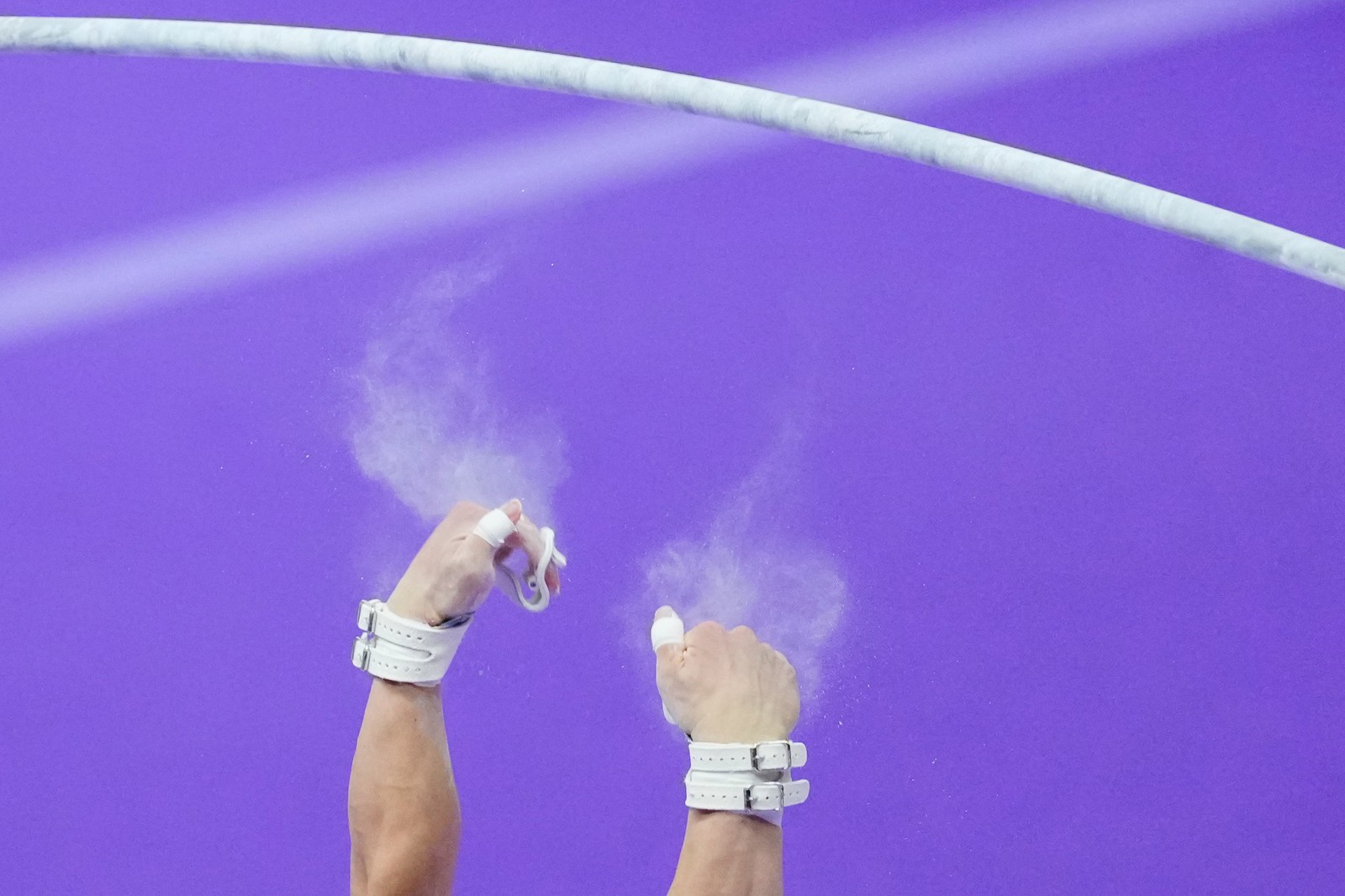 Chalk dust flies from the hands of a gymnast who just slipped off a bar during an exercise.