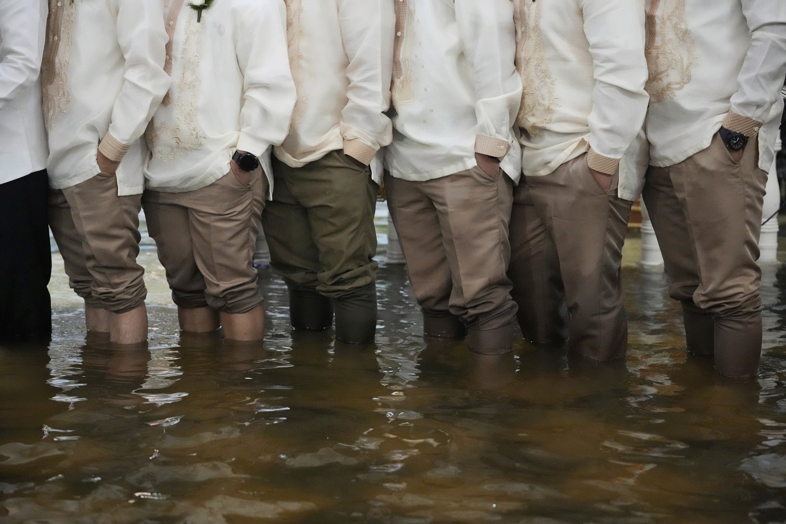 Groomsmen and guests with their pant legs rolled up stand in floodwater.