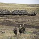 Three soldiers walking in front of a line of tanks