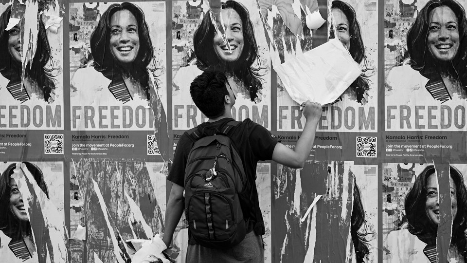 A black-and-white photo of a man tearing down a poster among a spread of identical posters depicting Kamala Harris and the word 'freedom.'
