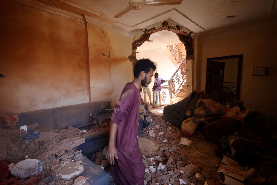 People stand and walk inside a heavily damaged room in a residential building.