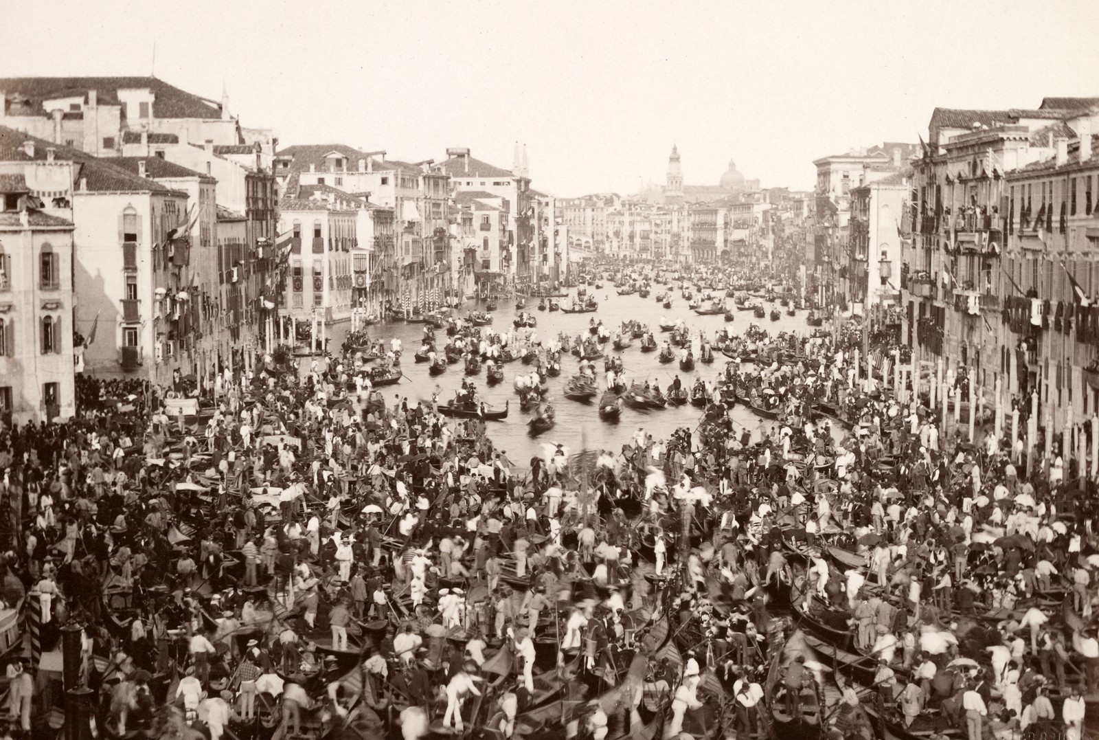 Hundreds of small boats and rowers cluster together in a broad canal in Venice.