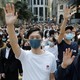 A crowd of Hong Kong protesters in masks raise their hands in unison.