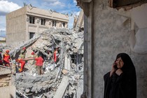 An image of a woman speaking on the phone as emergency workers sift through rubble of a residential building that was hit in an airstrike in Tehran.