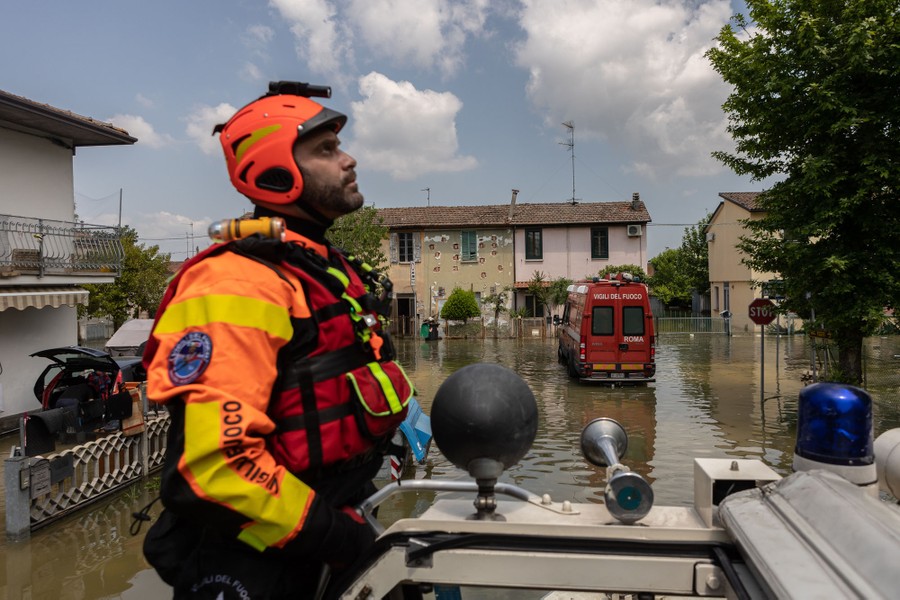 A firefighter stands on a vehicle as it patrols a flooded street.