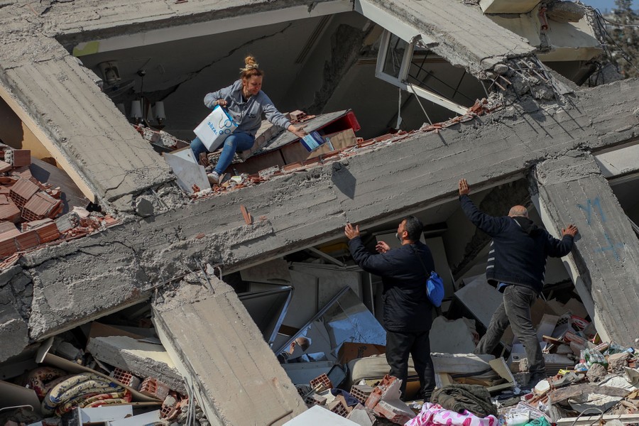 People remove small items from a pile of rubble that was formerly a residential building.