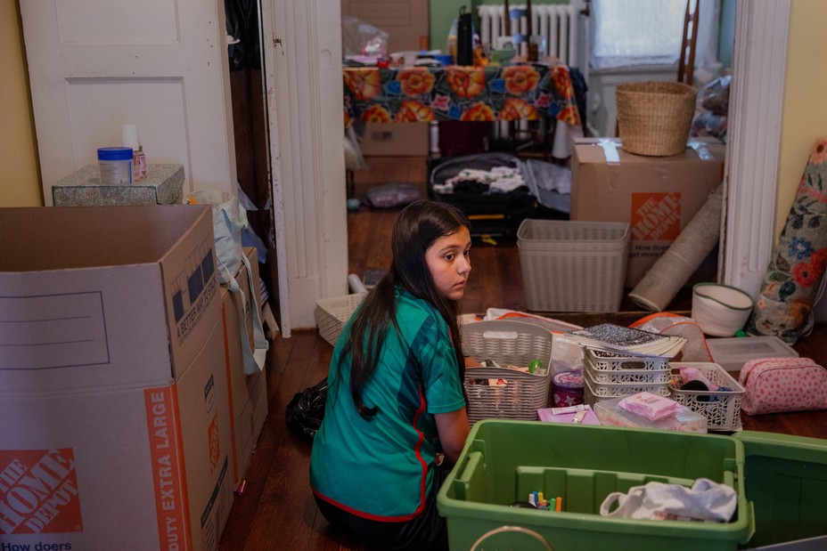 photo of young girl sitting on floor next to boxes and plastic crates in house while packing