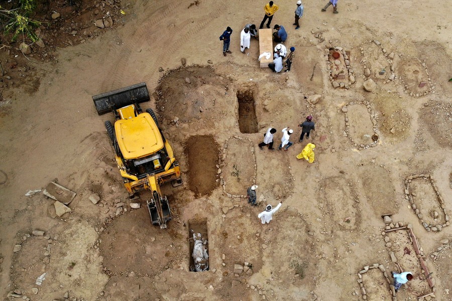 A view of an excavator and workers among several new graves in a cemetery.
