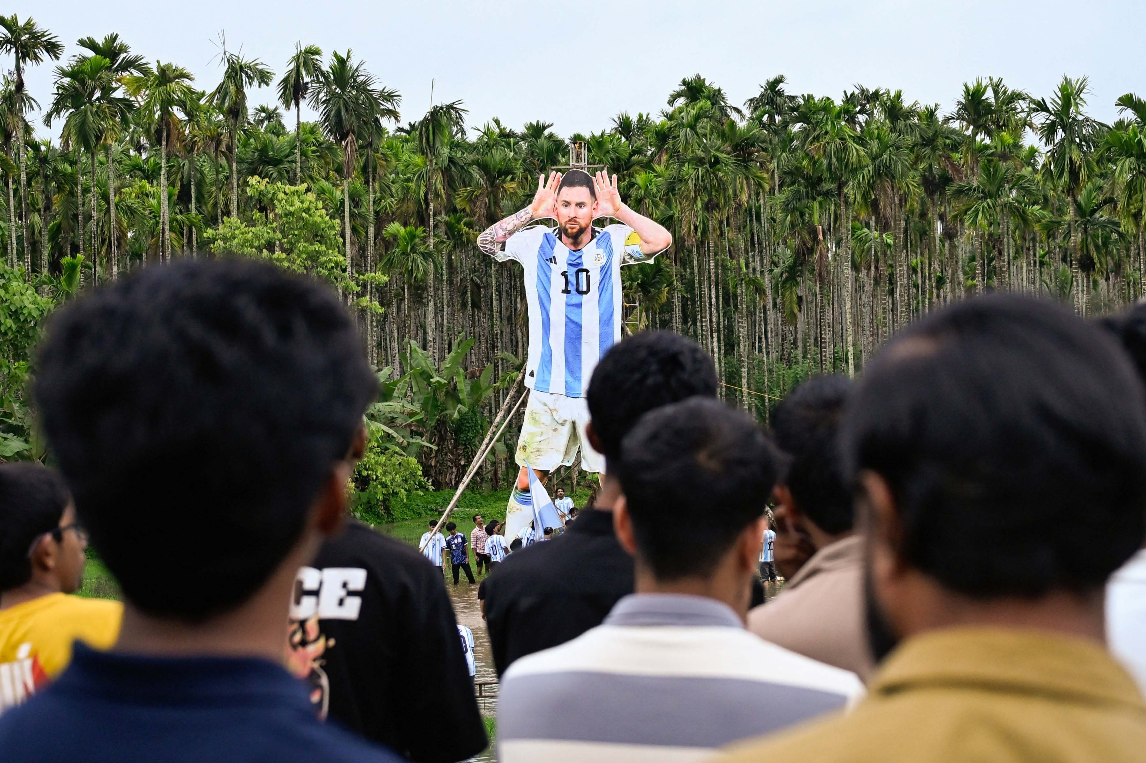 People look on as others stand up a tall cutout of Lionel Messi in a soccer uniform.