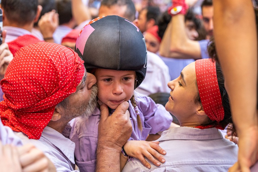 Two people hug and kiss an emotional girl who is wearing a helmet.