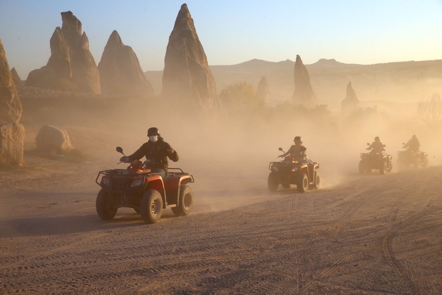 People ride ATVs near tall stone formations in a desert.