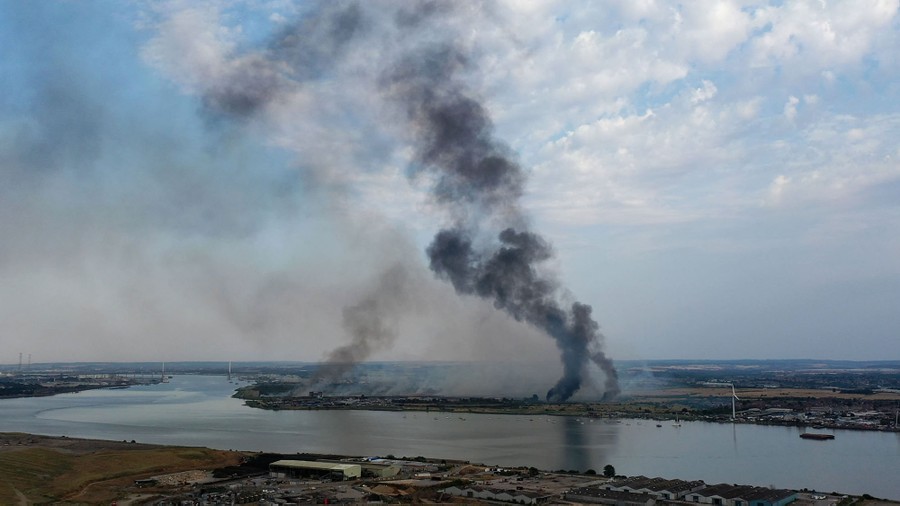 Black smoke rises from land near a broad river.