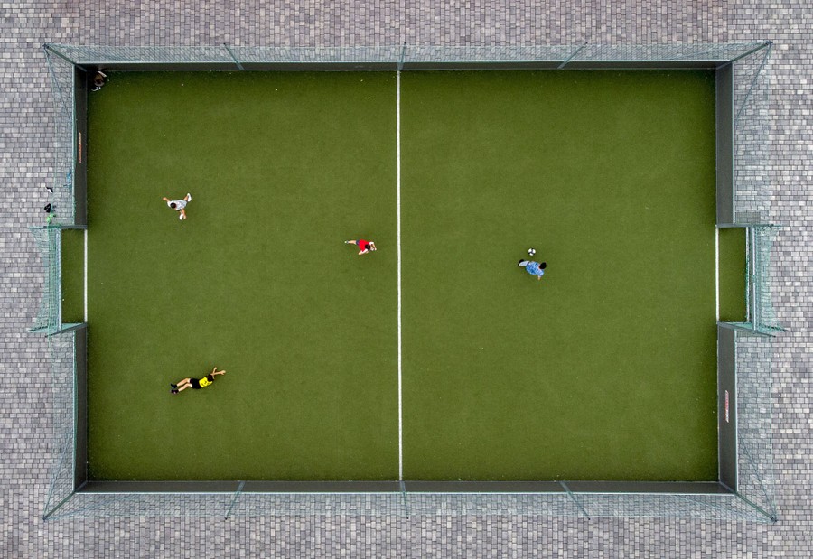 An aerial view of four children playing soccer on a small pitch.