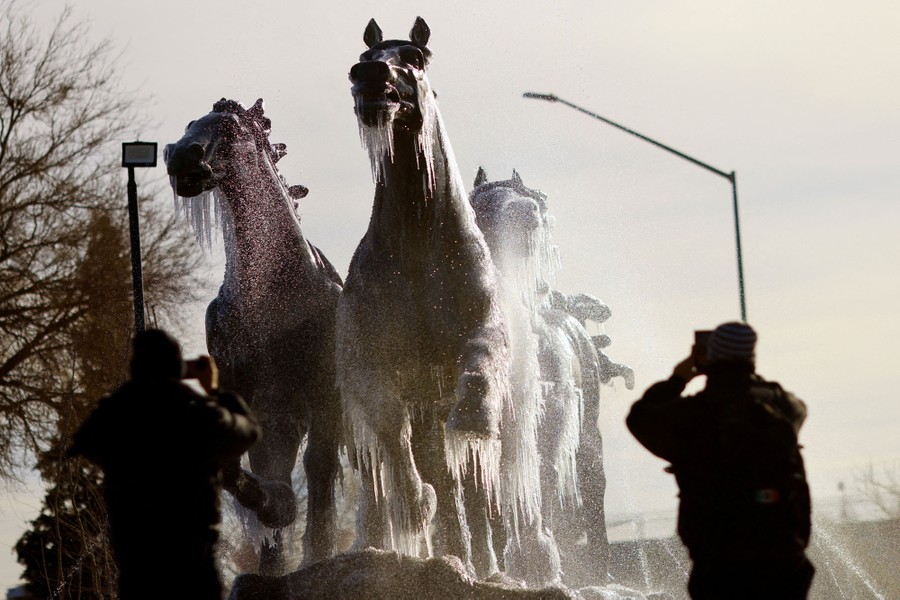 People take pictures of a sculpture of a herd of running horses, covered in icicles.