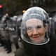 A woman wearing a protective helmet poses in front of a line of riot police during a protest.