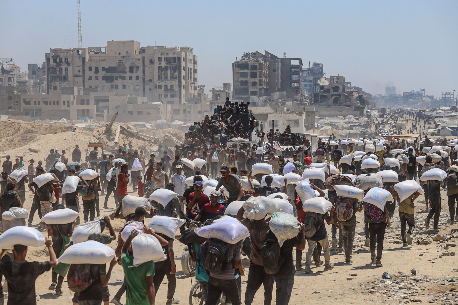 Hundreds of people can be seen in a long line, many of them carrying large bags of flour.