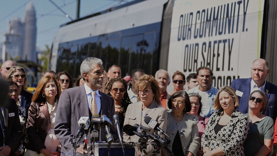 A man speaks at a podium at a press conference in front of a train that is displaying the words "Our Community. Our Safety."