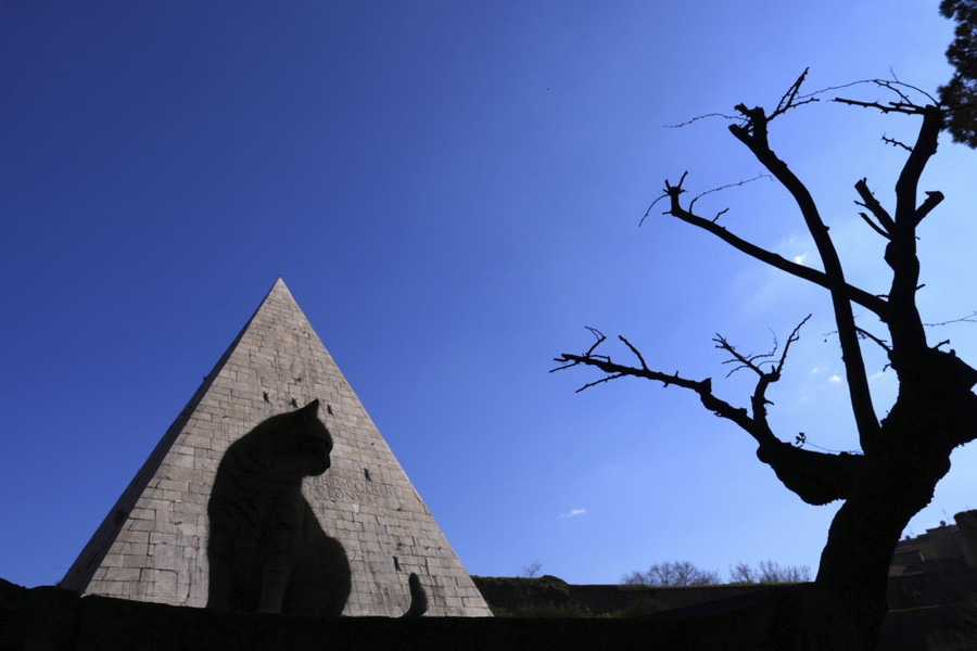 A cat in silhouette in front of a stone pyramid