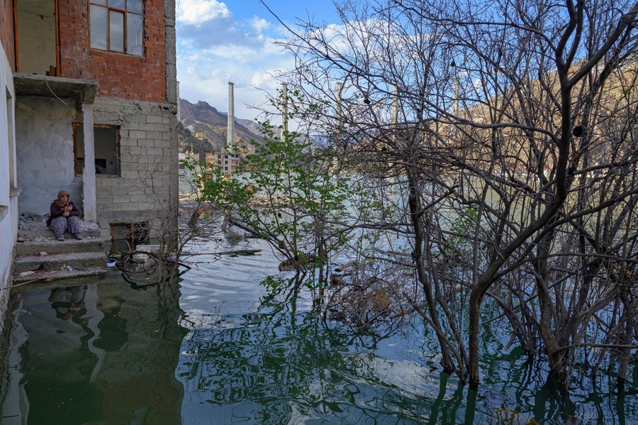 A person sits on the stoop of a flooded building.