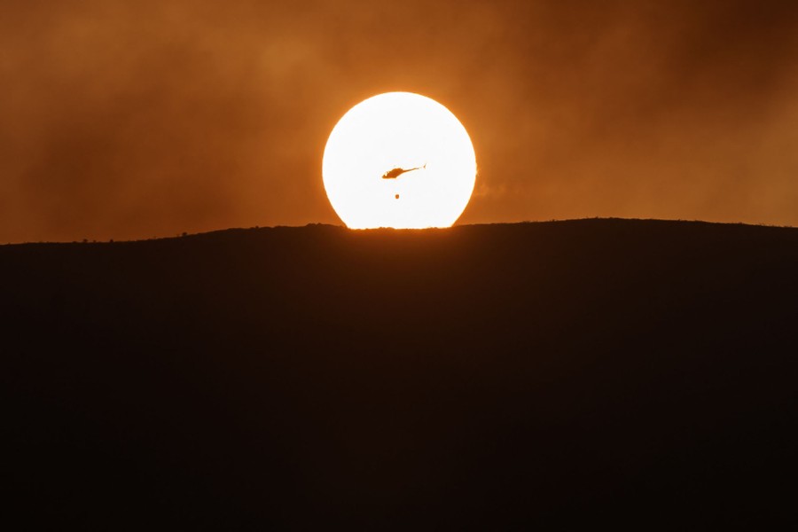 A helicopter carrying water flies with the sun in background.