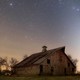 A photograph of an abandoned farm in rural Illinois at night, with the glow of zodiacal light overhead