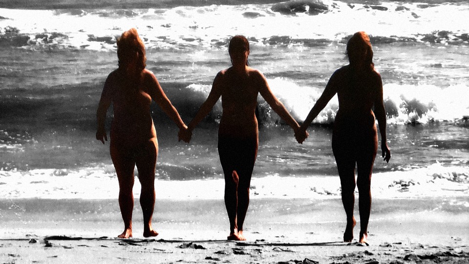 Three nude sisters hold hands on the beach.