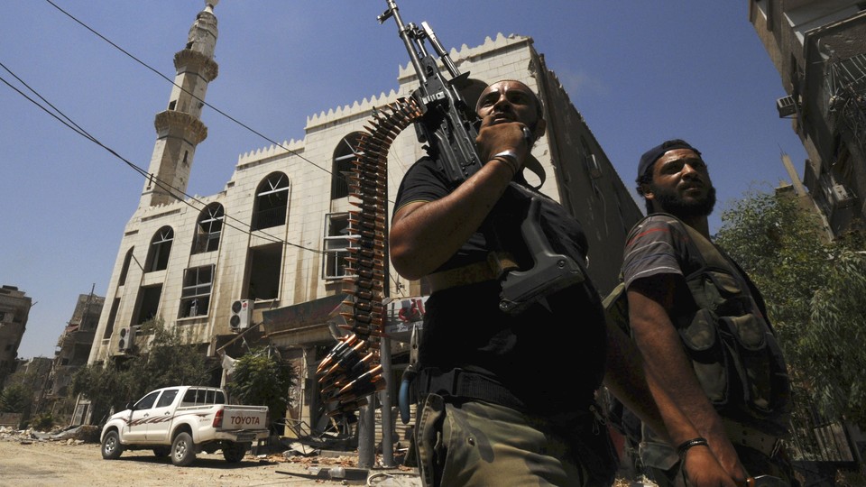 Two men with guns walk down a street in Syria.