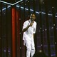 Chris Rock dressed in all-white onstage holding a microphone