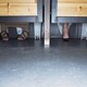 Two women sitting side by side in toilet stalls with their feet visible below the door