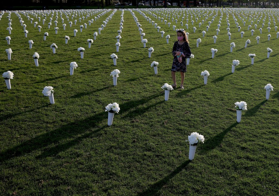A girl walks among thousands of flowers arranged in a grid.