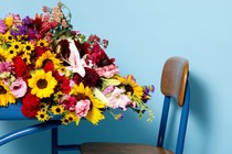 A profile view of a desk with flowers spilling off of it, against a blue background