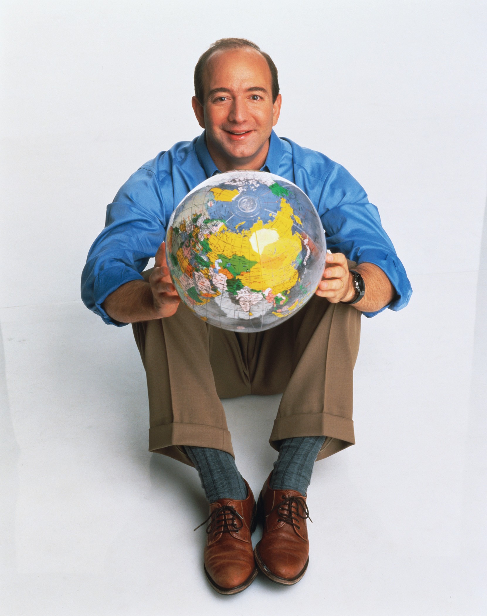 photo of Jeff Bezos seated on floor holding beach ball with map of the globe on it