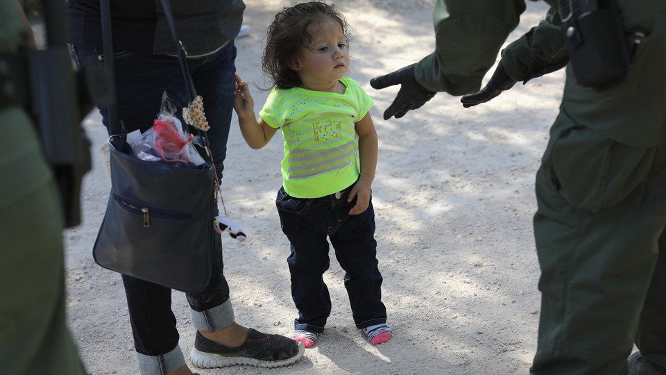 A small child looks at a border patrol agent as she and an adult, both asylum seekers, are taken into custody.