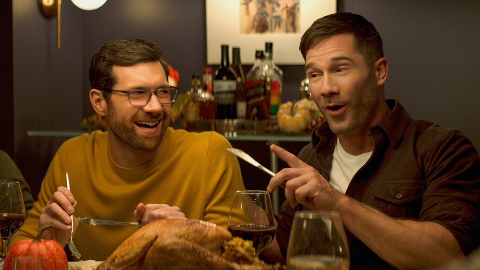 Billy Eichner and Luke Macfarlane laughing at a dinner table in "Bros"