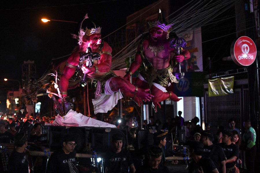 A group of people carry several frightening sculptures through a parade route at night.