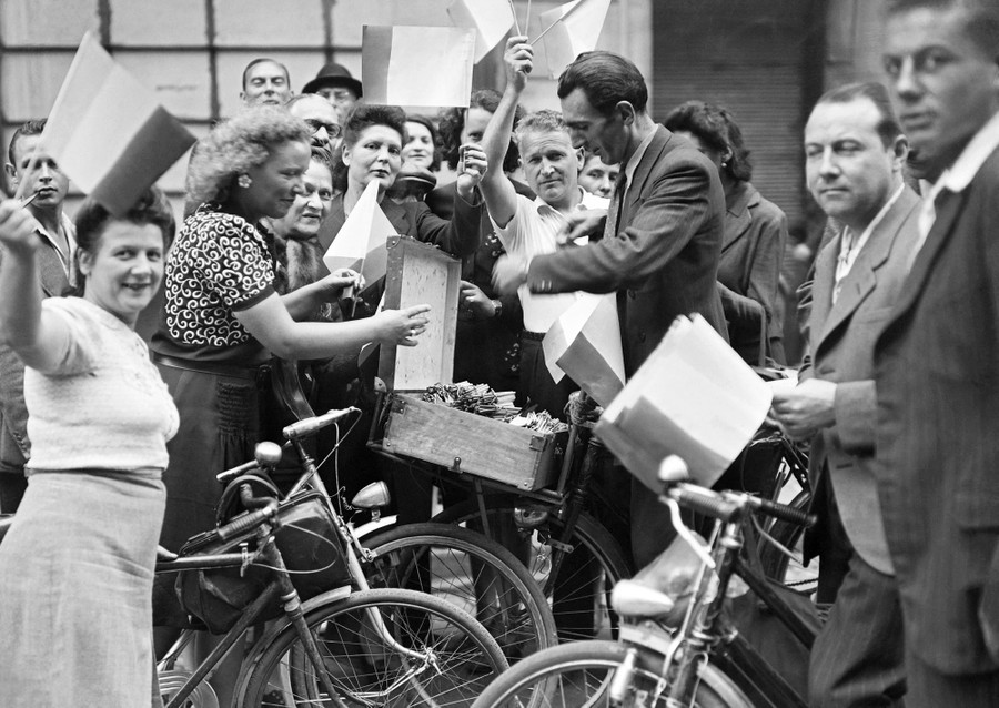 A crowd celebrates, buying small French flags from a seller with a box of flags attached to his bicycle.