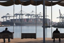 Men wait alone on benches at a port.