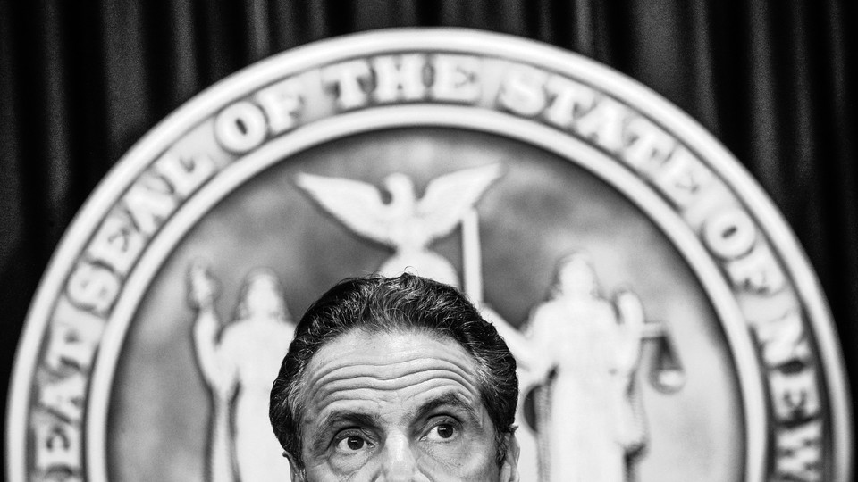 The top half of New York governor Andrew Cuomo's head is shown in front of the seal of the state of New York.
