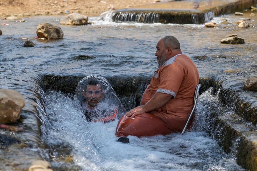 Two men cool off in a stream, one splashing water over his head.