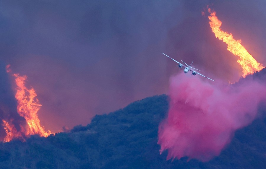 A firefighting aircraft drops a plume of fire retardant over a wildfire.