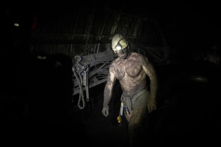 A shirtless miner, covered in coal dust, walks in a mine.