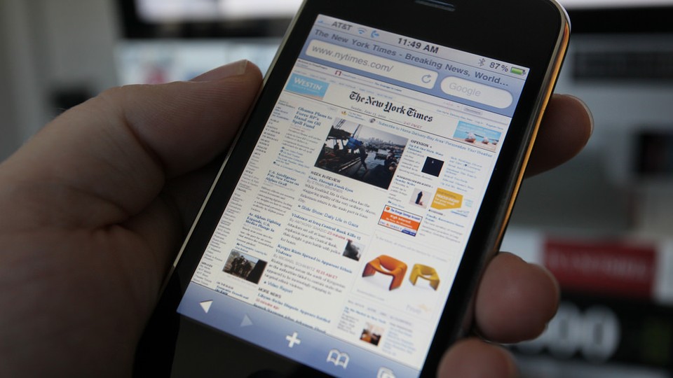 A left hand holds an iPhone with The New York Times' homepage displayed on the screen.