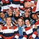 group photo of 10 astronauts in space station, some upside down, most wearing matching red, white, and blue polo shirts