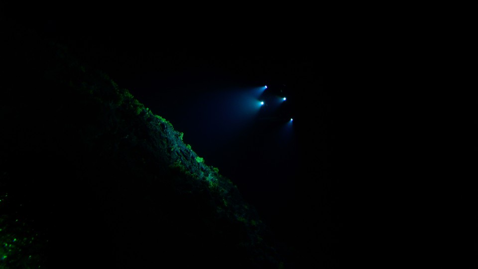 The lights of a submarine shine on a rock deep underwater.