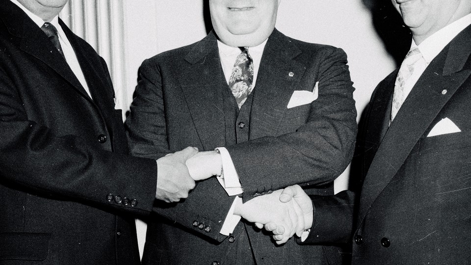 Black-and-white photo of three men shaking hands in suits
